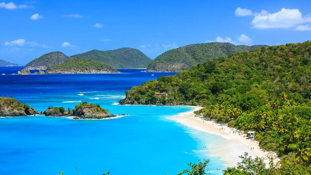 A coastal beach with clear turquoise waters, lush greenery, and a small structure on the beach.