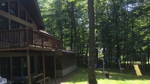 Une terrasse en bois avec un espace salon couvert et un toboggan dans un jardin arboré.