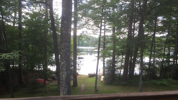 Une terrasse en bois avec un banc et un thermomètre. Au fond, on aperçoit un lac entouré d’arbres.