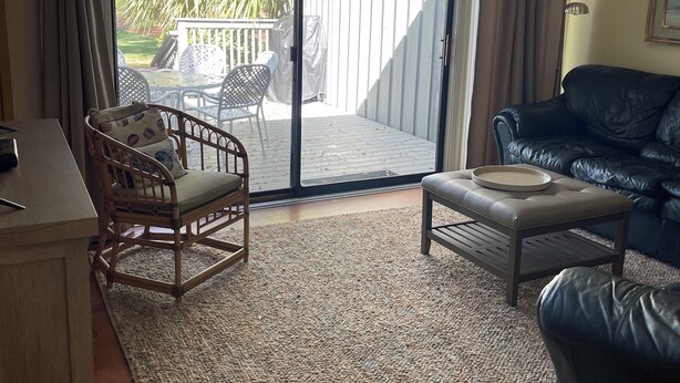 Ein Wohnzimmer mit einer Schiebetür zu einer Terrasse, einem schwarzen Ledersofa, einem Holzstuhl, einem kleinen Tisch und einem Holzbüro.