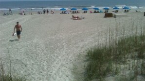 Ein sandiger Strand mit Menschen, Sonnenschirmen und Liegestühlen.