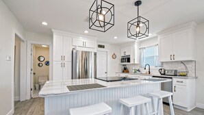 A modern kitchen with white cabinetry, a central island with bar stools, and pendant lighting. - Beautifully Remodeled - Short Walk to Beach! (Gulf Shores)