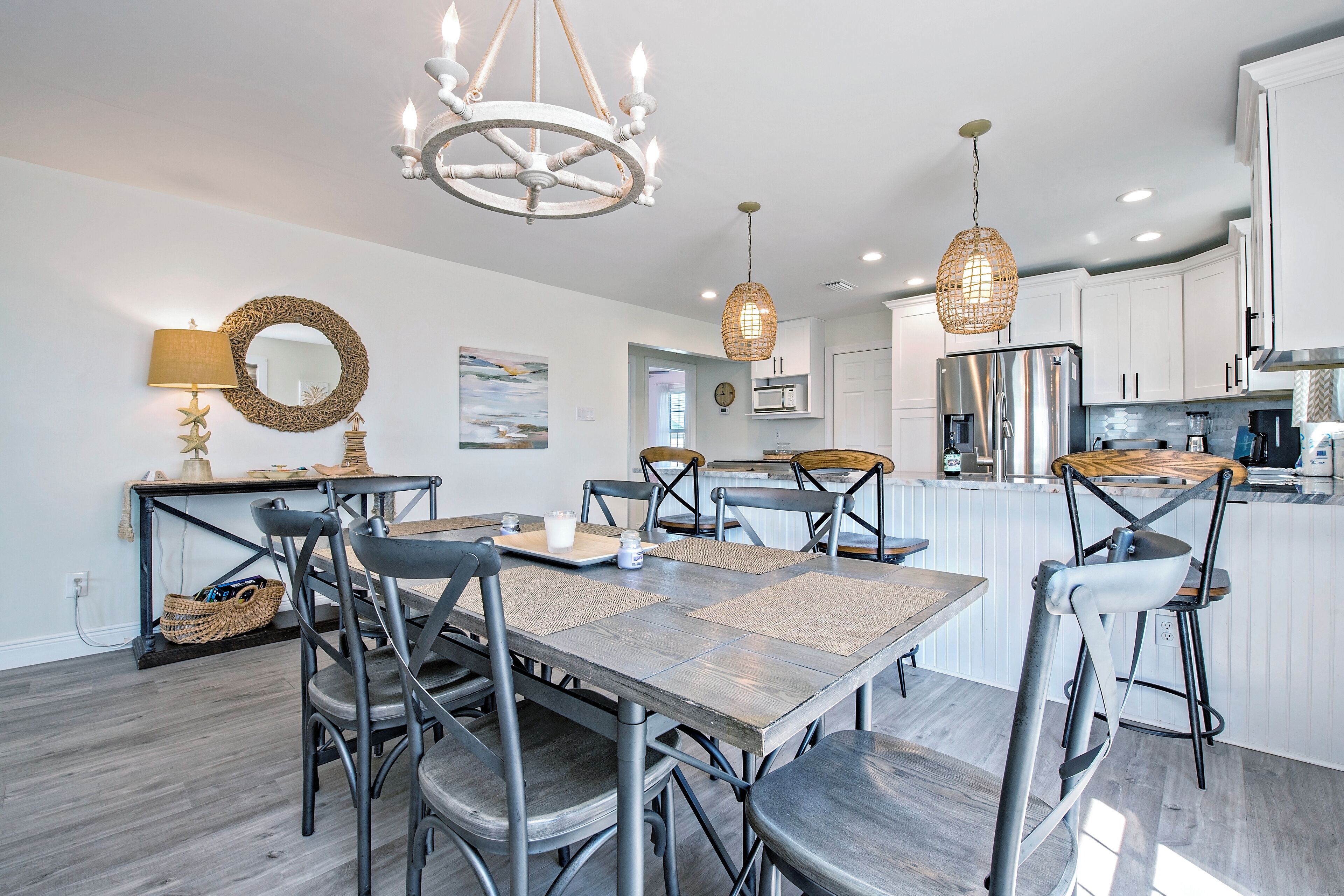 Een moderne keuken met witte kastjes, roestvrijstalen apparatuur en een eethoek met een houten tafel en metalen stoelen.