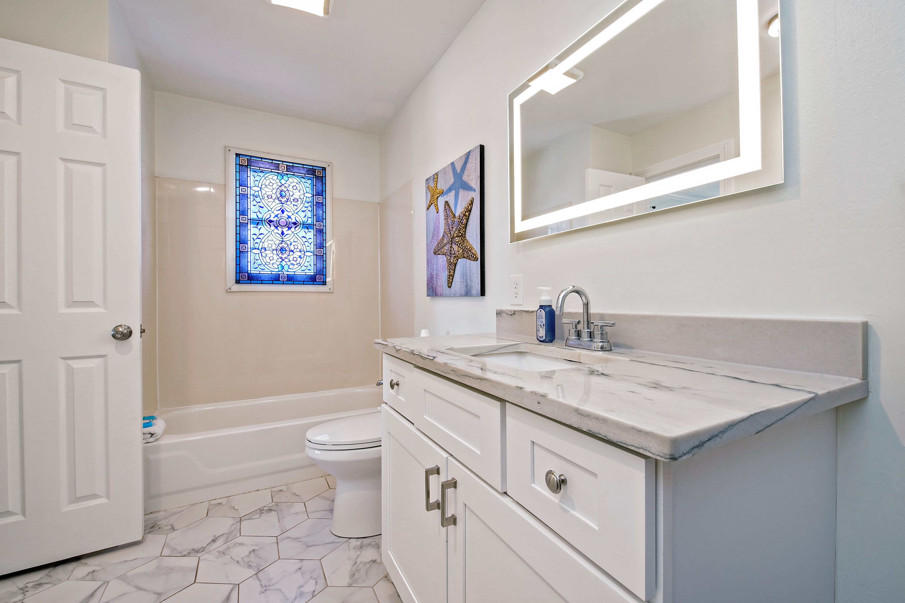 A bathroom with a white vanity, a large mirror, a bathtub, and a toilet.