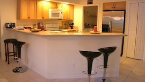 A kitchen with wooden cabinets, a microwave, a stove, a refrigerator, and a bar area with stools. - Villa Salva, Your Home Away From Home! (Cape Coral)