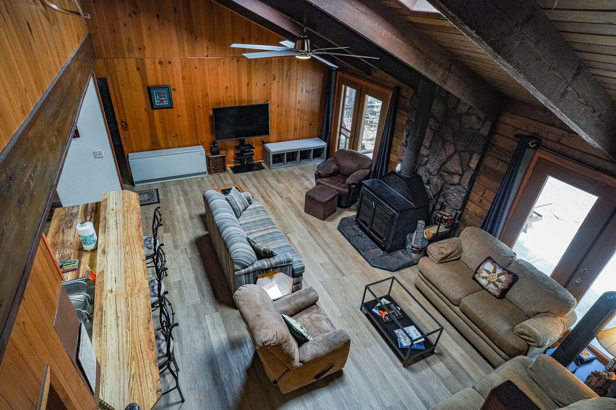 A cozy cabin interior with a wooden floor, a sofa, a recliner, a fireplace, and a television.