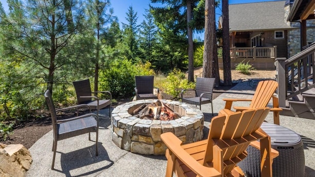 An outdoor seating area with a stone fire pit, surrounded by chairs and a view of a building with a balcony.