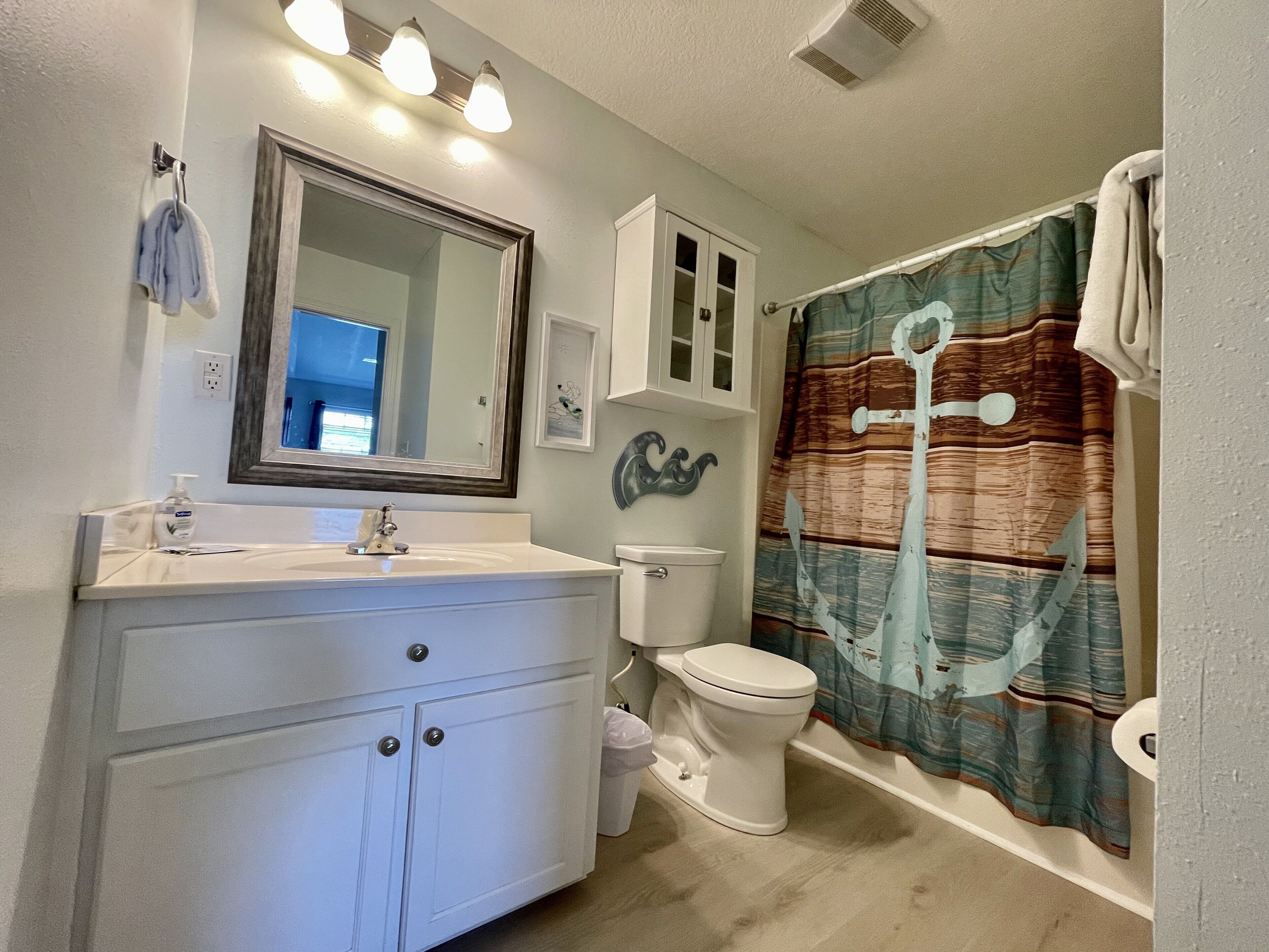 A bathroom with a white vanity, a toilet, a shower curtain, and a mirror.