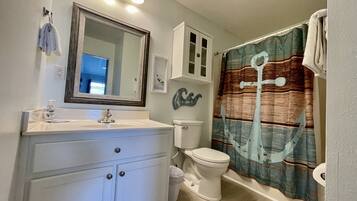 A bathroom with a white vanity, a toilet, a shower curtain, and a mirror.