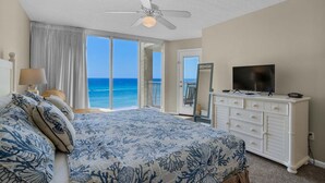 A bedroom with a bed, a TV, a dresser, and a view of the ocean.