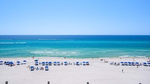 A beach with white sand, clear blue water, and numerous blue umbrellas.