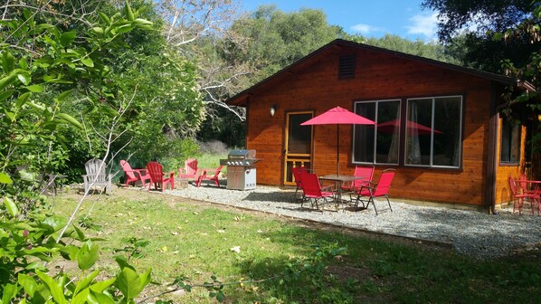 Una cabaña de madera con un patio amueblado con sillas rojas y una parrilla.