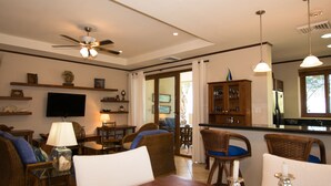 A dining area with wicker furniture, a television, and a ceiling fan.