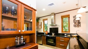 A kitchen with wooden cabinets, a black countertop, stainless steel appliances, and a window with a view of greenery.