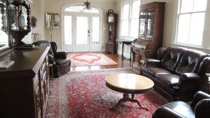 A spacious living room with a large red patterned rug, leather sofas, a wooden coffee table, and a ceiling fan.