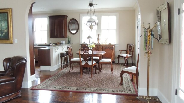 A spacious dining area with a wooden table and chairs, a chandelier, and a kitchen in the background.