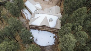 Una casa con tetto spiovente, circondata da fitti pini e un cortile innevato.