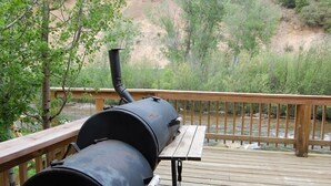 A barbecue grill on a wooden deck with a river view.