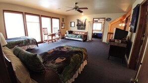 A room with two beds, a desk, a chair, and a ceiling fan.