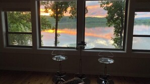 A room with a large window overlooking a lake and trees, two stools, and a chair. - Secluded getaway on Lake Catherine, minutes from town - birds, fishing, & kayaks (Hot Springs)