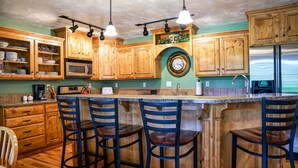 A kitchen with wooden cabinets, a microwave, a clock, and a stainless steel refrigerator. - Blue Spruce Inn 1.25 acres mountain views 6 bed 6.5 bath 4,040 sqft (Victor)