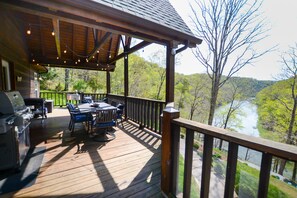A wooden deck with a grill, outdoor seating, and a view of a river.