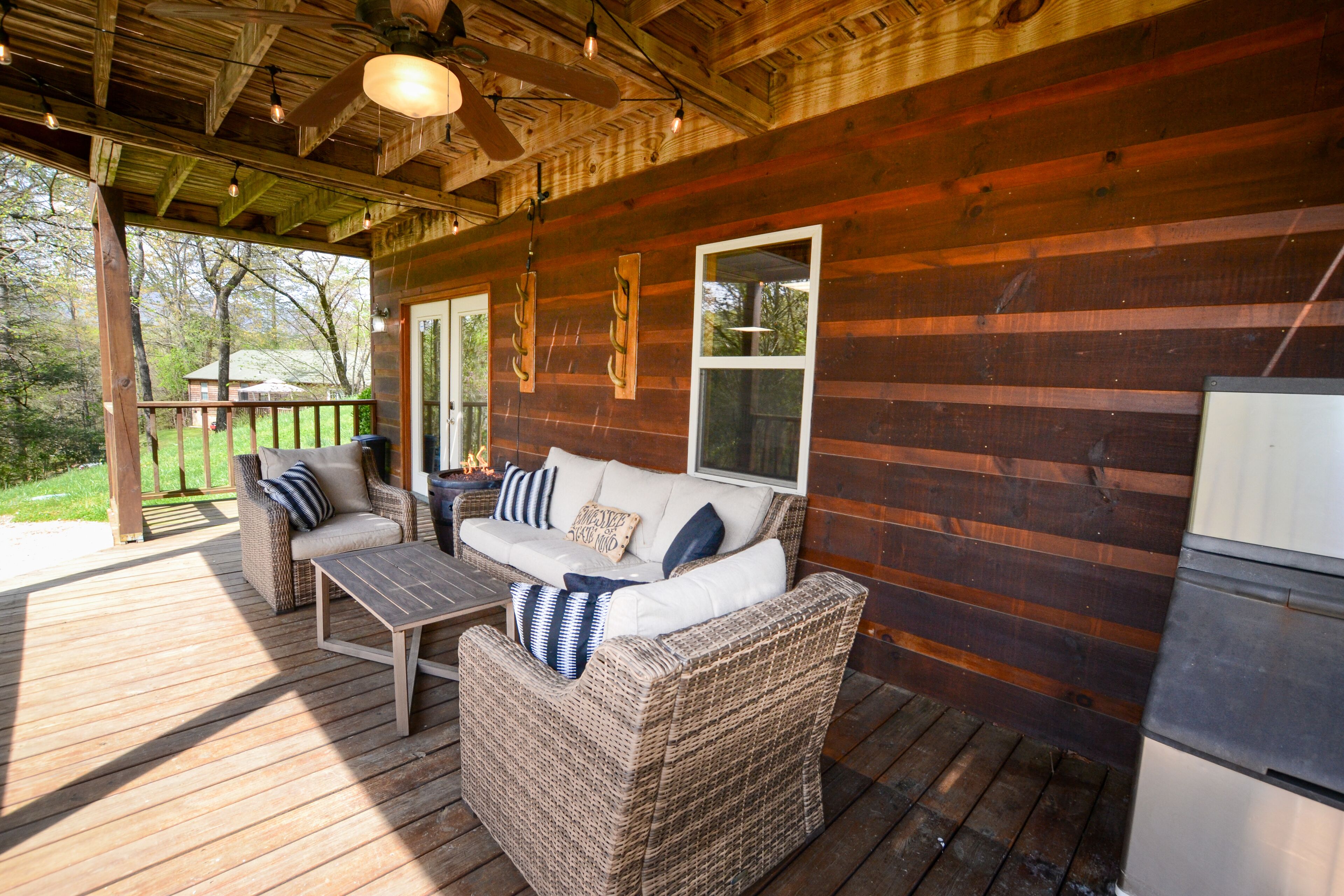 A covered porch with wicker furniture, a table, and a refrigerator.