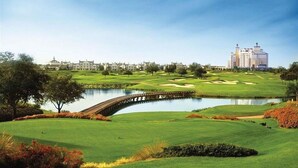 Un parcours de golf avec un étang, un pont en bois et un hôtel en arrière-plan.