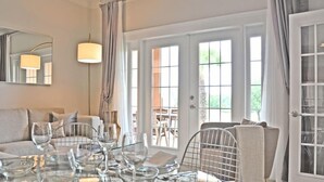 Un vaste salon comprenant un coin repas avec une table en verre dressée pour le repas, un canapé et une grande fenêtre agrémentée de rideaux.