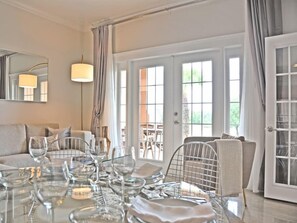 Enjoy meals in style at this spacious living area with a dining table set for a meal, offering a view of the outdoors through a large window.