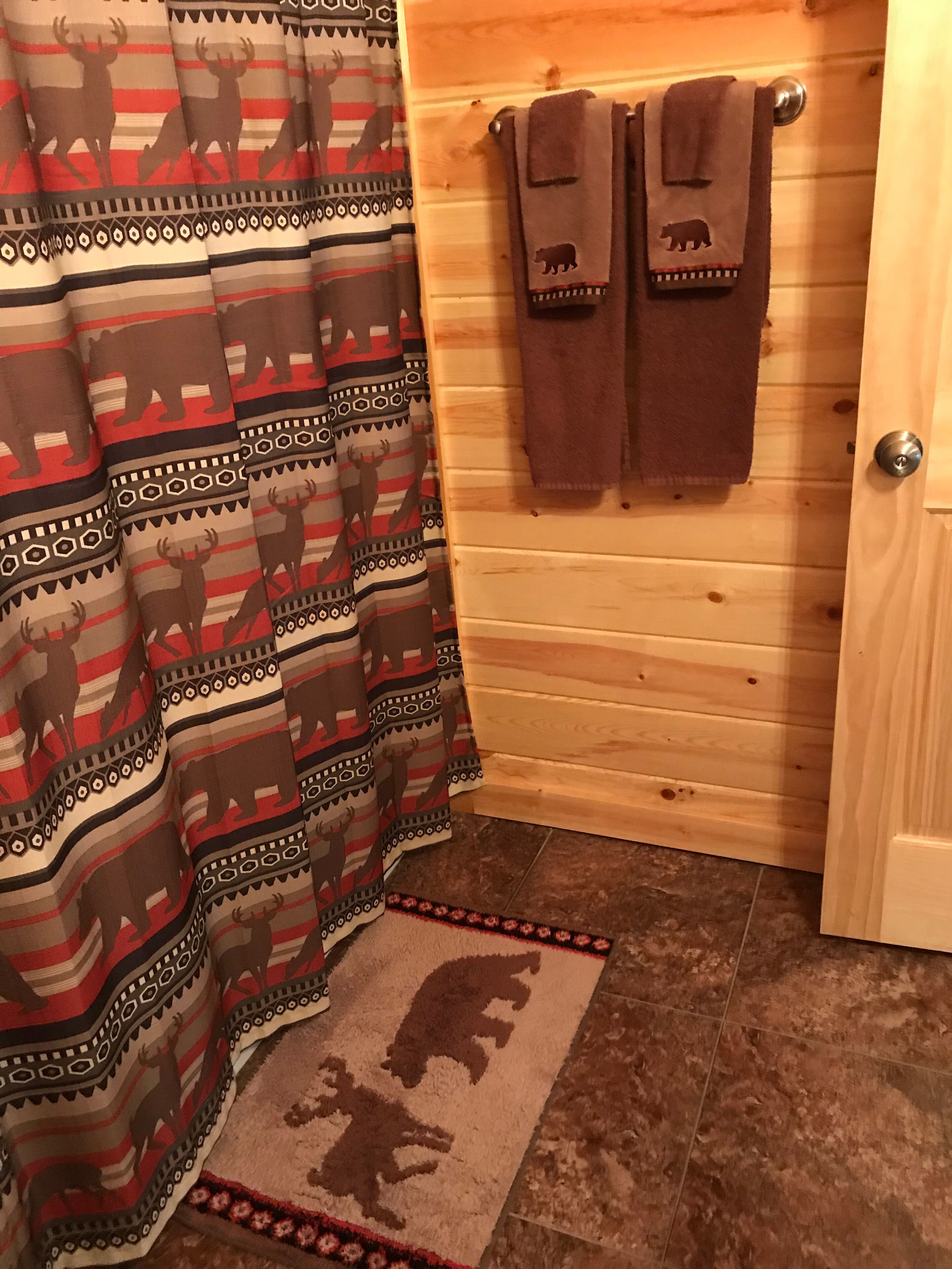 Ein Badezimmer mit einem waschschrankartigen Duschvorhang, einem Teppich mit Tierkonturen und Handtüchern, die an einer Holztür hängen.