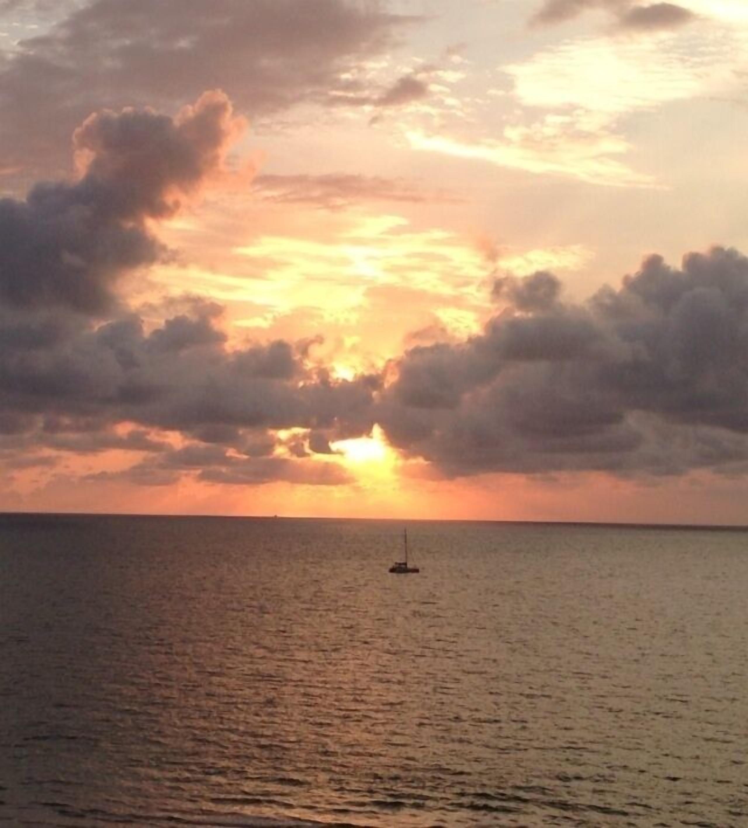 Un coucher de soleil sur une mer calme, avec un seul bateau à l'horizon.