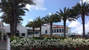 Edifici amb façana blanca i teulat vermell, envoltat de palmeres i un massís floral amb flors blanques i vermelles.