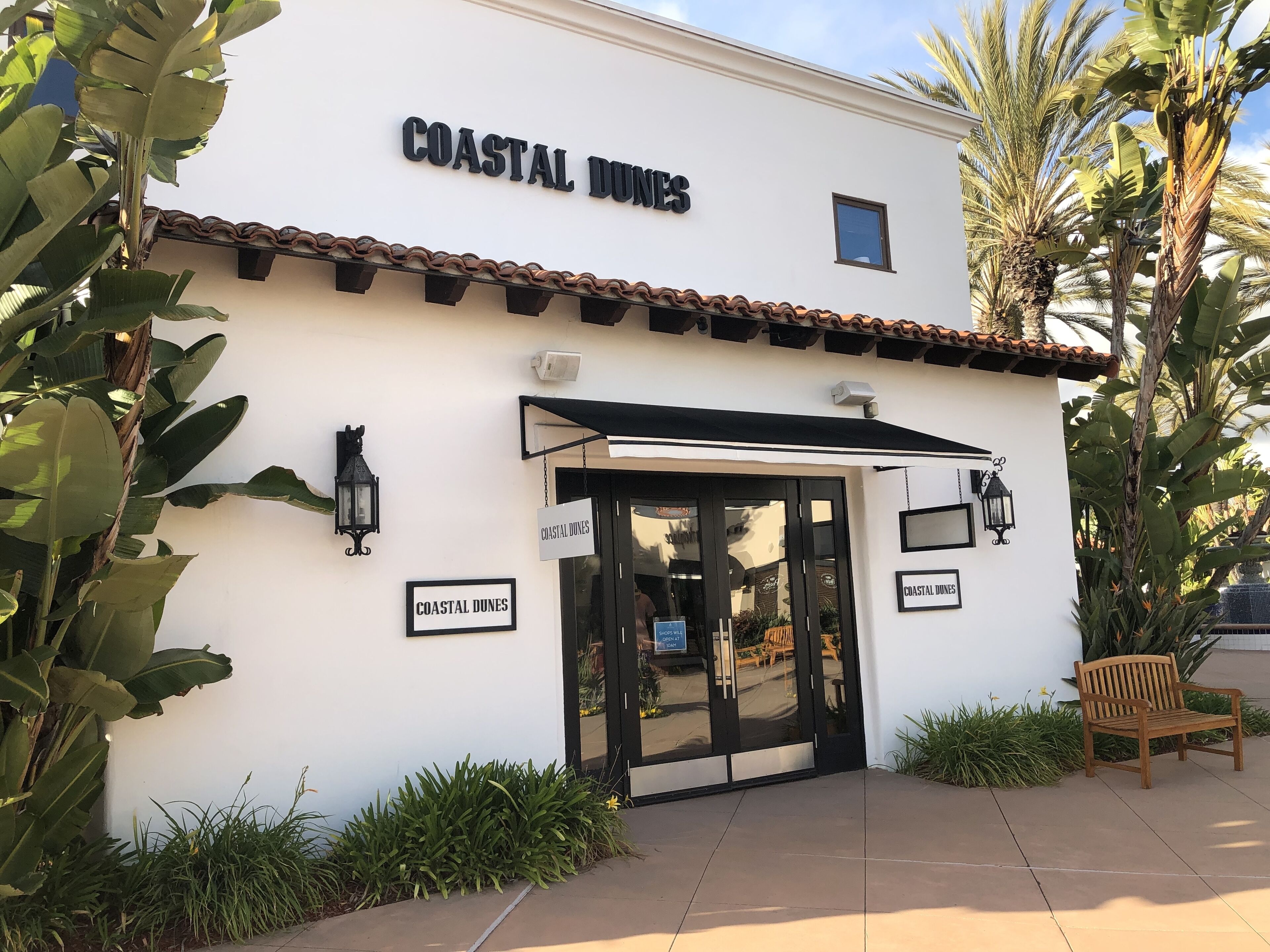 A building with a sign reading "COASTAL DUNES" and a bench outside.