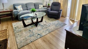 A modern living room with a grey sofa, armchairs, a glass coffee table, and a flat-screen TV.