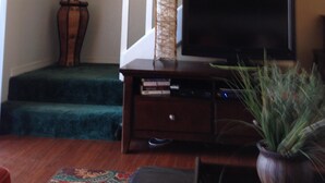 A living room with a staircase, a television on a wooden stand, a large potted plant, and a framed picture on the wall.