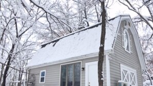 A small, single-story house with a sloped roof, a front door, and a garage door. - The Garden Cottage. (Stilwell)