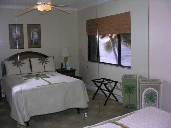 A bedroom with a bed, a nightstand, a lamp, a window with a view of palm trees, and a ceiling fan. - Fabulous Kona Reef Resort Ocean Front - Penthouse Floor - 2 BR/2 BA Condo (Kailua-Kona)
