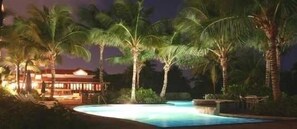 A nighttime scene of a resort with a swimming pool surrounded by palm trees and a building with a lit exterior. - LOCATION! Beach & Ocean Front Luxury Villa Rio Mar Resort (Rio Grande)
