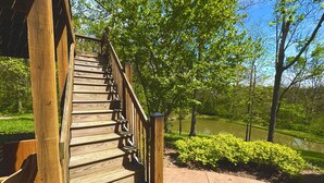 Una escalera de madera que conduce a un edificio con vistas a un estanque y vegetación.