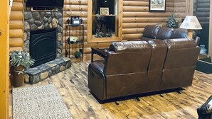 Ein rustikales Blockhaus-Interieur mit Kamin aus Stein, einer Ledersofa und einem wandmontierten Fernseher.