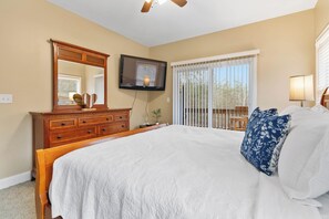 Ein Schlafzimmer mit einem großen Bett, einem Holzschrank, einem an der Wand befestigten Fernseher und einem Fenster mit Jalousien.