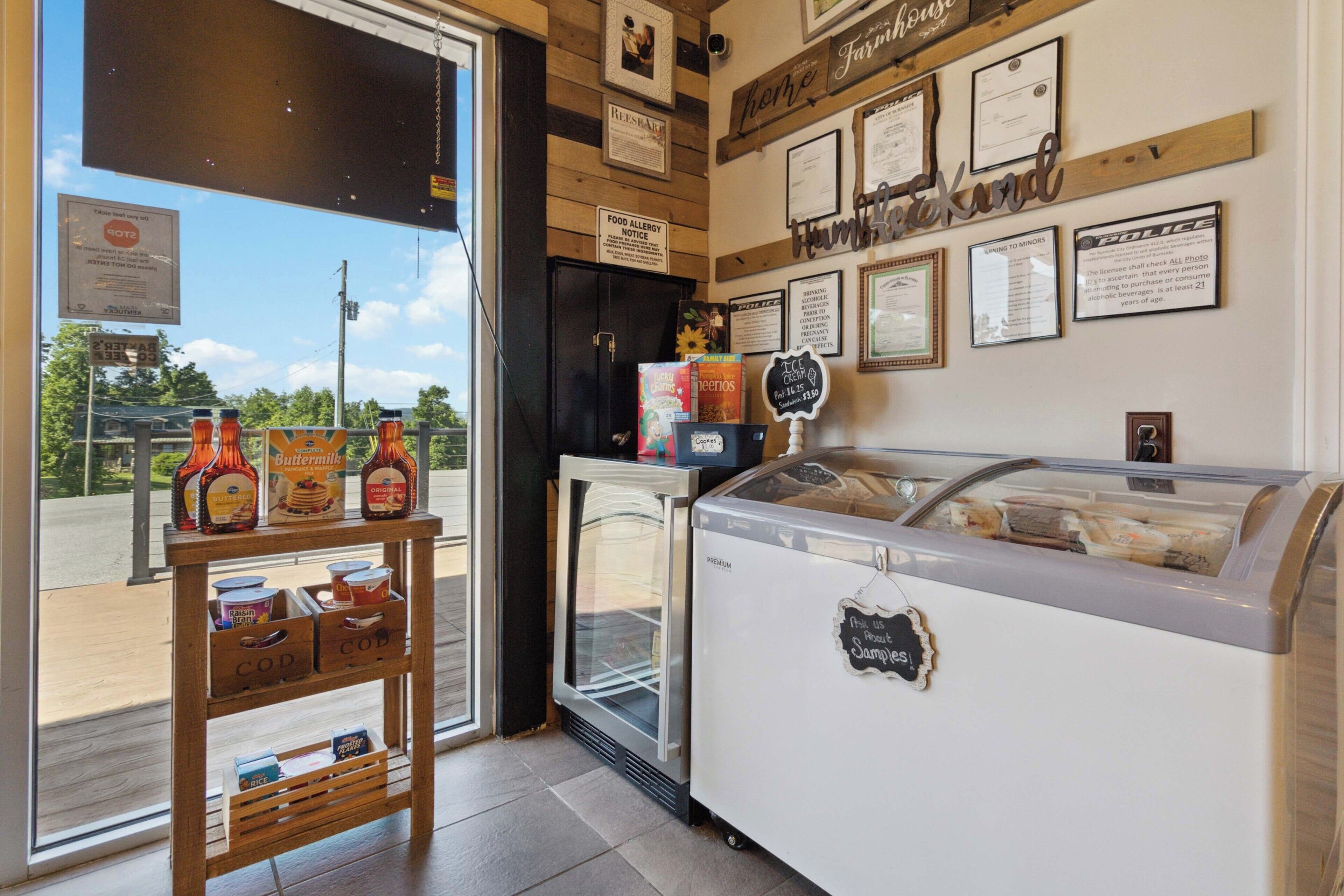 A bakery with a display case, a refrigerator, and a wooden shelf with condiments.