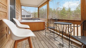 Una terraza de madera con un jacuzzi, dos sillas blancas y una mesa metálica con sillas.