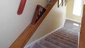 Una escalera con barandilla de madera, un aplique de pared y un cuadro enmarcado.