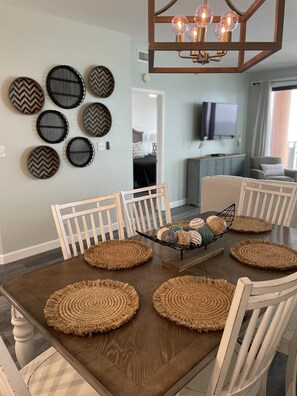 A dining area with a wooden table, white chairs, woven placemats, and decorative plates on the wall. - Seachase 1404 West Sun, Fun, and Plenty of Room!! (Orange Beach)