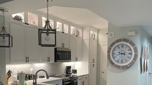 Eine moderne Küche mit weißen Schränken, einer großen Kochinsel mit Barhocker, Edelstahlgeräten und einer großen Wanduhr.