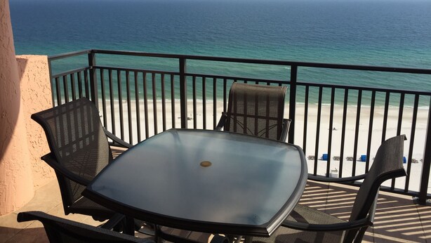 Ein Balkon mit Glastisch und zwei Stühlen, der Blick geht auf einen Strand und den Ozean.