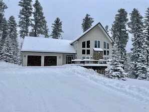 Een tweelaags huis met een garage, omringd door met sneeuw bedekte bomen.