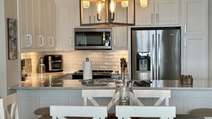 A modern kitchen with white cabinetry, stainless steel appliances, a central island with a glass top, and a chandelier. - IP 616-Completely Renovated, Luxury Ocean Front 3bdrm/3bath (Fort Walton Beach)